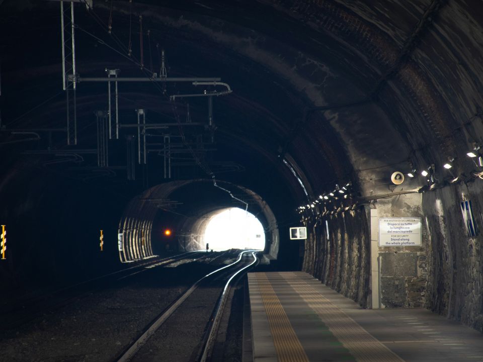 Electric train travelling through a lit rail tunnel at night, with overhead electrification equipment