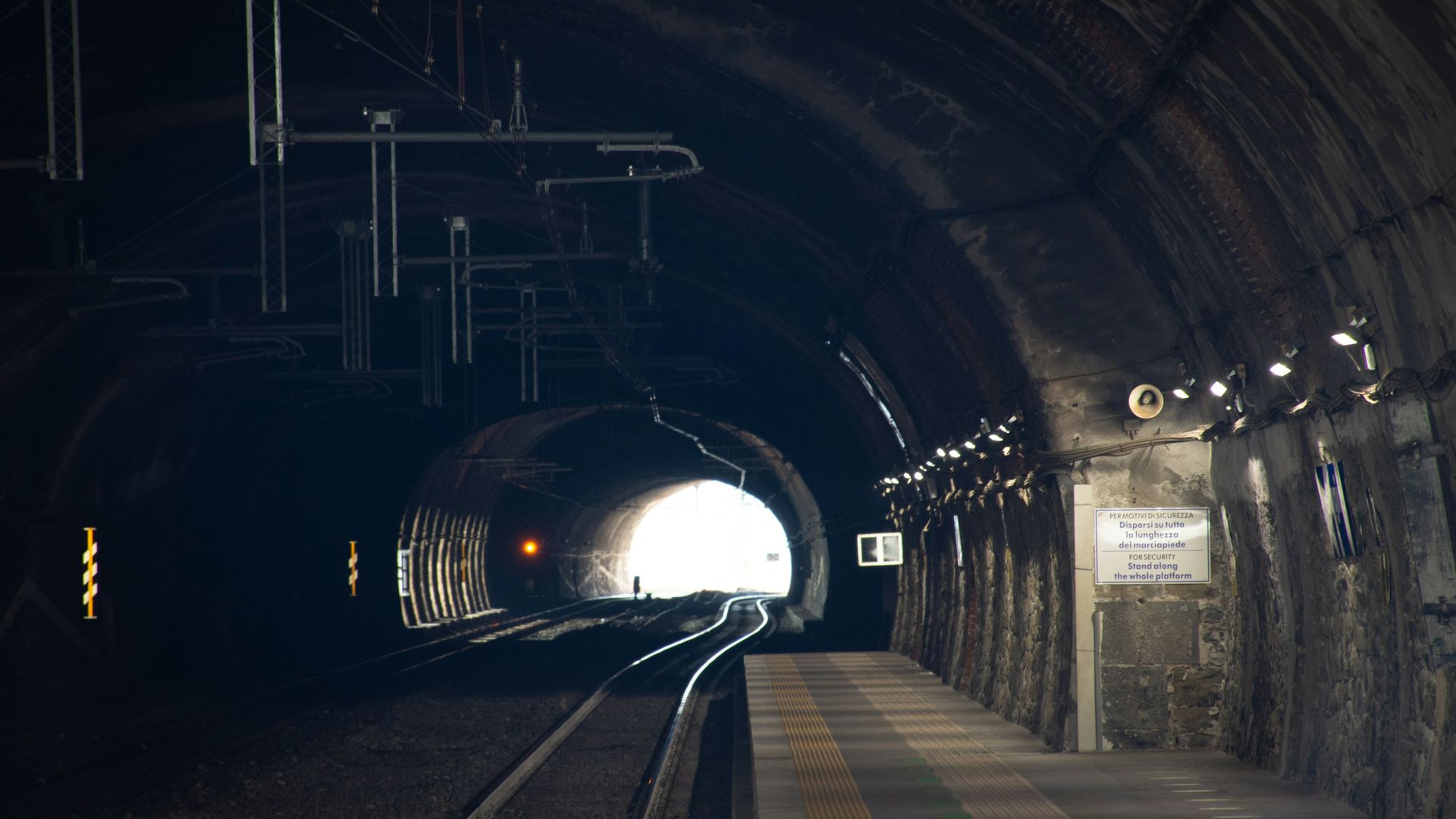 Electric train travelling through a lit rail tunnel at night, with overhead electrification equipment