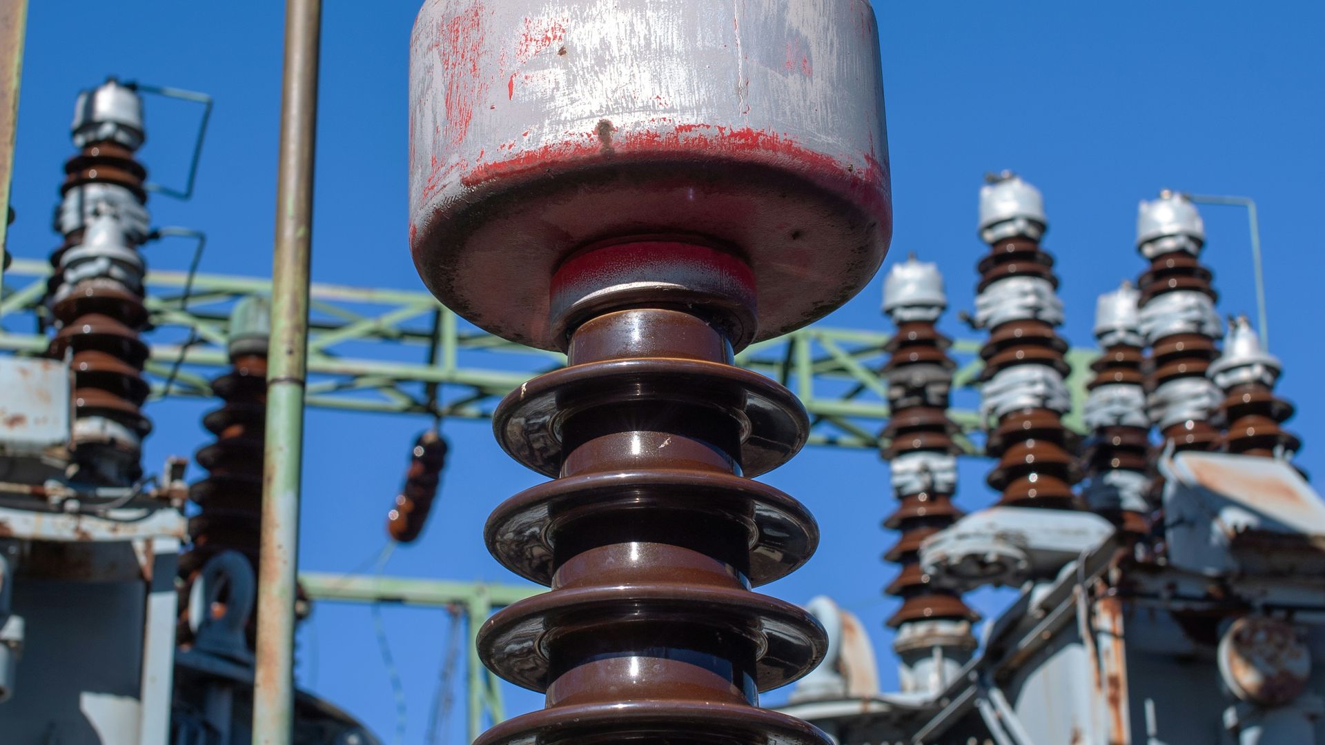 Close-up of insulator stacks at a high-voltage substation, with transformers behind